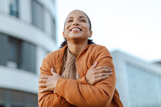 Give yourself a hug Beautiful African-American woman in orange jacket smiling and enjoying in the city hugging self stock pictures, royalty-free photos & images