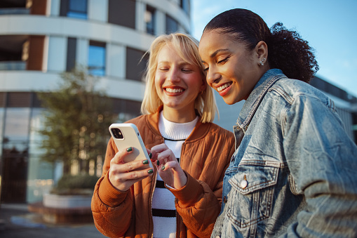 Two young women hanging out in the city and using smart phone