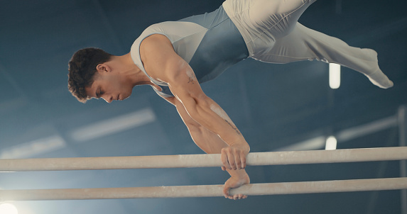 Sports man, fitness and gymnastics performance by olympic  athlete at gymnasium for exercise, training or workout. Health motivation, commitment and gymnast on parallel bars at Argentina competition