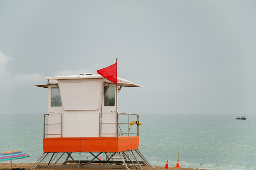 Lifeguard on rescue post at sandy beach near sea with green flag. Lifeguard searching sea areal. Safe vacation concept. Clean endless beaches. Copy space.