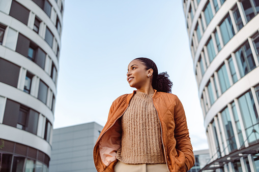 Beautiful African-American woman in orange jacket smiling and enjoying in the city