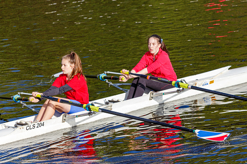 Chester Le Street UK 05/13/2015\n\nCloe-up of two girls dressed in red holding oars and rowing in the river, sunny day with reflections in the water