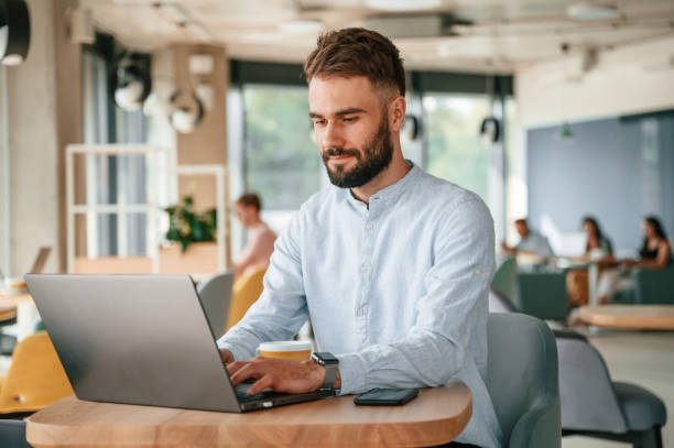 istock Young man is sitting in the cafe and working by using laptop 1438608926