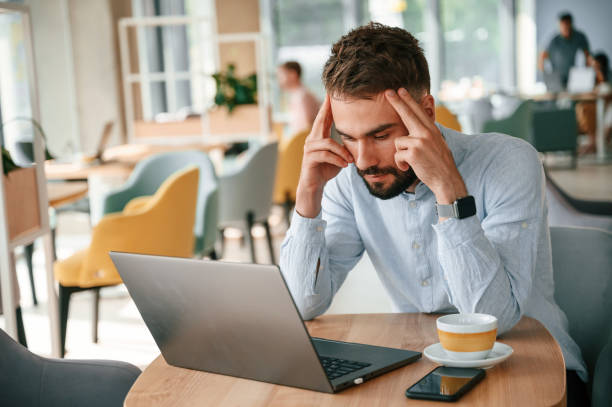 istock Feeling bad and tired. Young man is sitting in the cafe and working by using laptop 1438609013