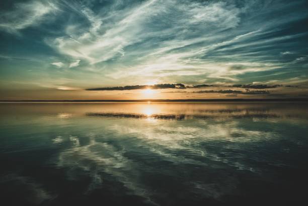 istock Setting sun and the clouds of the sky reflected in the ocean below 1438611069