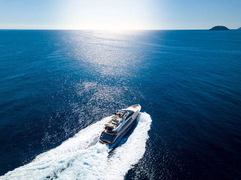 An aerial shot of a yacht sailing on the sea under a blue sky