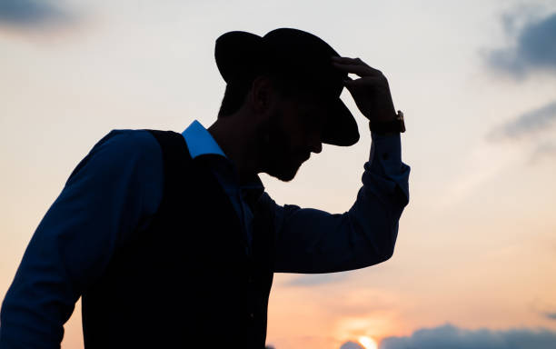 istock man dancer silhouette pose with hat against sunset sky, silhouette 1438611623