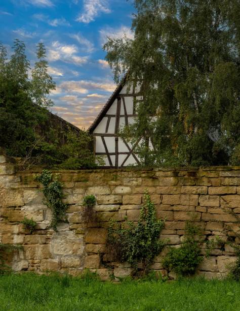 old half-timbered house behind an old quarry stone wall with trees and a great sky