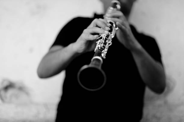 Grey scale shot of a person playing clarinet in front of a white wall A grey scale shot of a person playing clarinet in front of a white wall clarinet stock pictures, royalty-free photos & images