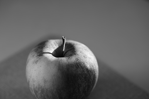 A greyscale of an apple reflecting on the table with a blurry background