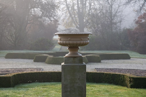 A selective focus shot of a stone pot on a pedestal in a park