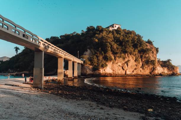 Beach surrounded by the sea and rocks covered in greenery with a bridge in Brazil A beach surrounded by the sea and rocks covered in greenery with a bridge in Brazil corcovado stock pictures, royalty-free photos & images