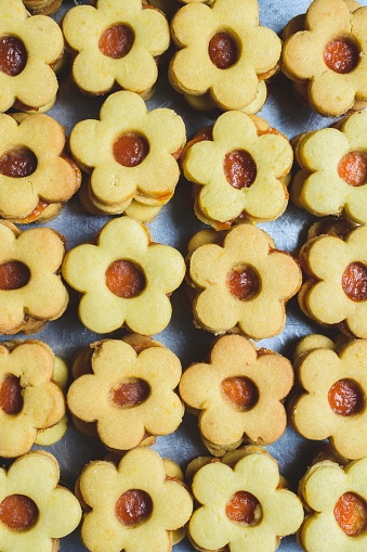 A vertical shot of many flower-shaped cookies with jam