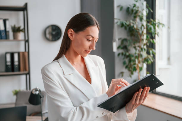 istock Reading document in notepad. Young beautiful woman in formal clothes is working at office 1438618959