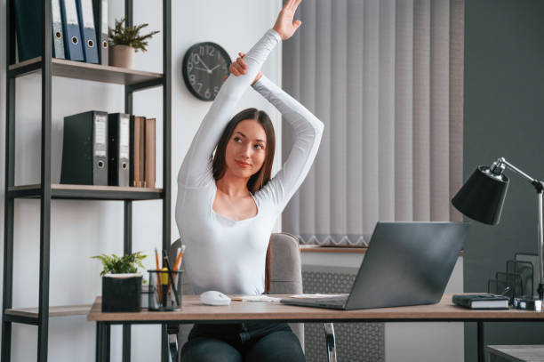 istock Doing exercise break. Young beautiful woman in white clothes is in the office 1438619086