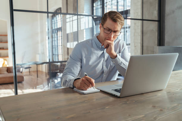istock Businessman at office in front of laptop, making notes in notepad, planning meetings with investors 1438619132