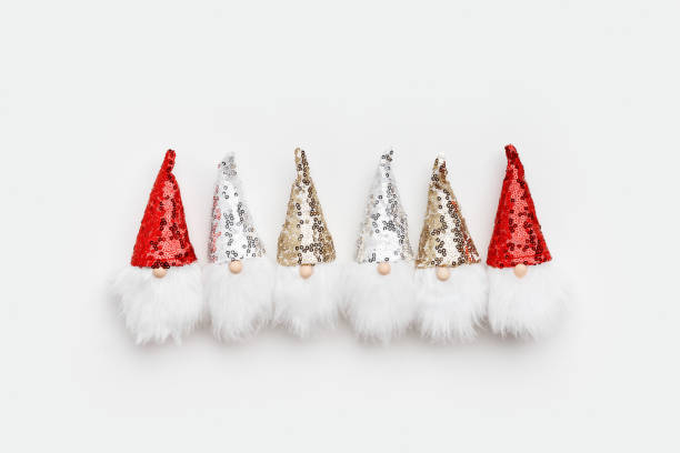 istock Christmas concept. Row Cute dwarfs with white beard and glittering red gold silver sequins on cap white background. Christmas, New Year background. Flat lay, top view minimal holiday pattern 1438619887