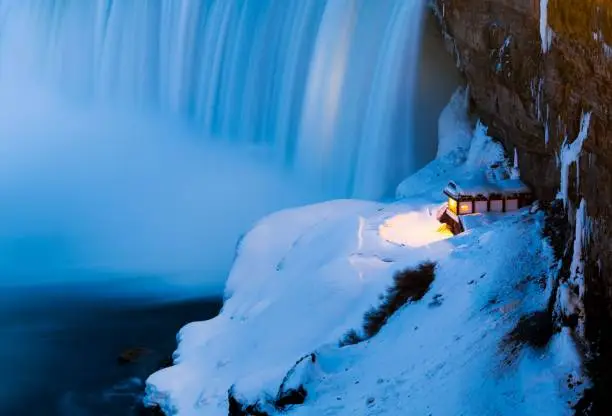 Photo of High angle of a house on a slope of a mountain with warm light in winter against a waterfall
