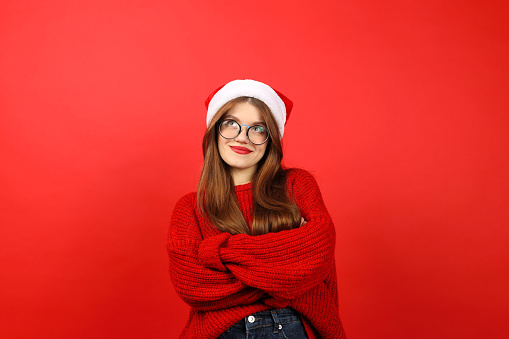 A girl in a red New Year's sweater and a santa hat makes a decision. Think about choosing a gift for Christmas.