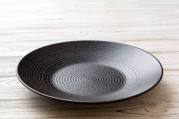 istock Perspective view of empty black plate on wooden background. Empty space for your design 1438622353