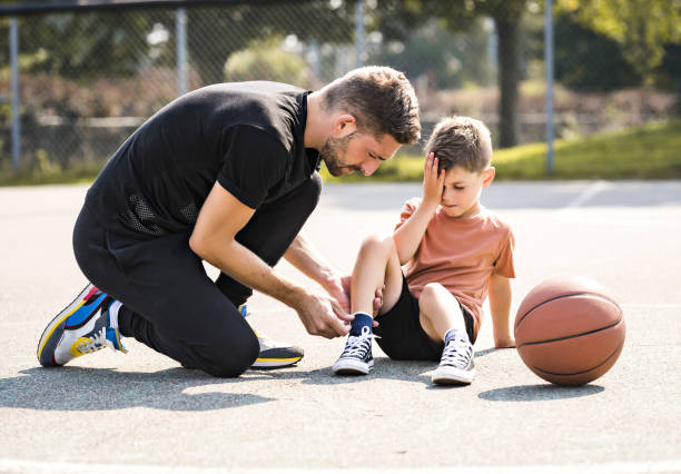 uomo e ragazzo che giocano a basket su un campo, il ragazzo ha lesioni alla caviglia e piange - athlete coach basketball male foto e immagini stock