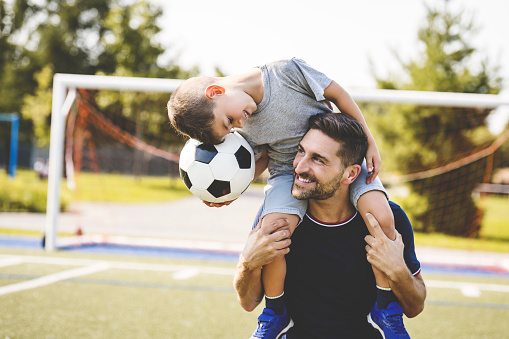 A man with child playing football outside on field