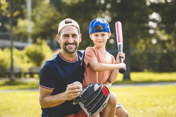 père et fils jouant au baseball par une journée ensoleillée au parc public - baseballs baseball sport summer photos et images de collection