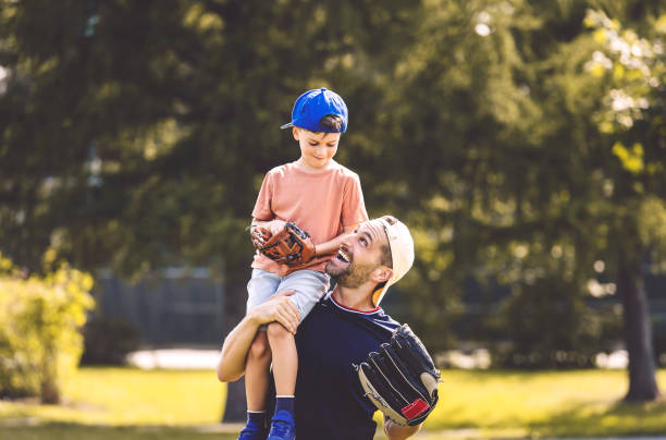 padre e figlio che giocano a baseball in giornata di sole al parco pubblico - padre foto e immagini stock