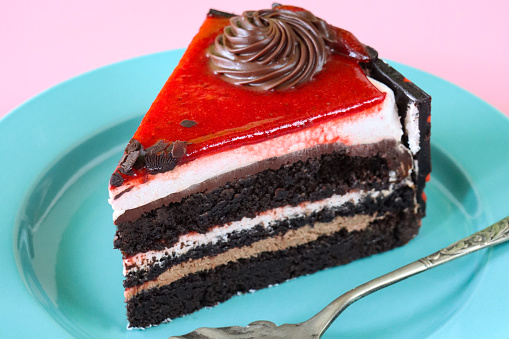 Stock photo showing close-up view of a slice of chocolate and cherry cake displayed on a plate against a pink background.