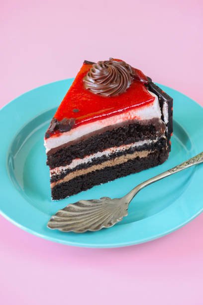 Stock photo showing close-up view of a slice of chocolate and cherry cake displayed on a plate against a pink background.