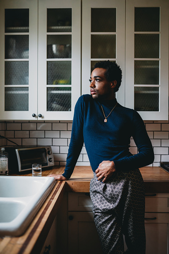 A non-binary person is standing in the kitchen. African american ethnicity.
