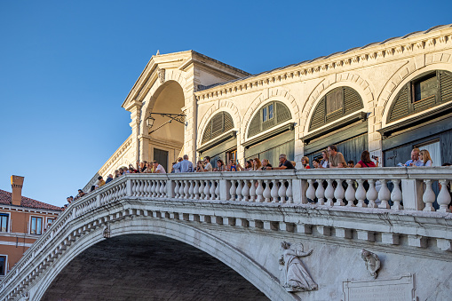 Venice, Italy - October 7th 2022:  Tourists in the late afternoon sun standing on the Rialto Bridge in the center of the old and famous Italian city Venice