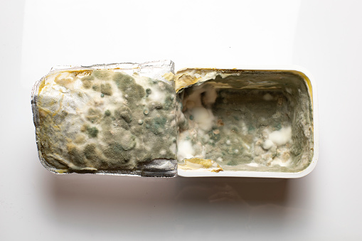 Processed cheese packaging with bacteria and mold gray green yellow color, plastic packaging with the remains of spoiled cream cheese close-up