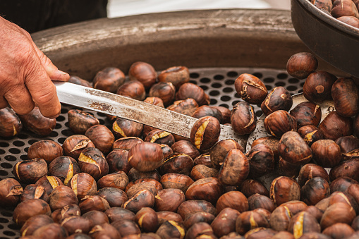 Roasting chestnuts in a bowl or grill on an open fire in a street food market, close up