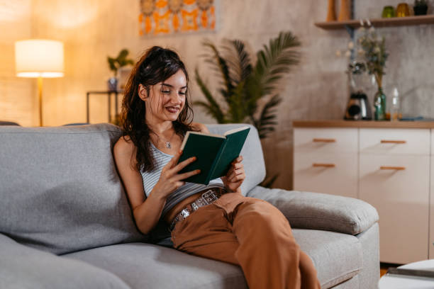 istock Young Woman Sitting On The Sofa And Reading A Book 1438632177