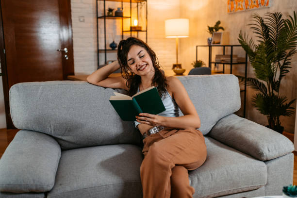 istock Young Woman Sitting On The Sofa And Reading A Book 1438632253