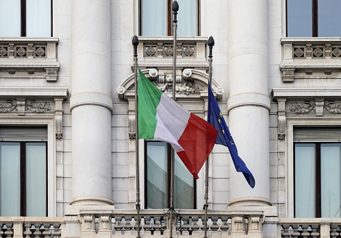 The flags of Italy and the European Union next to each other attached to a building