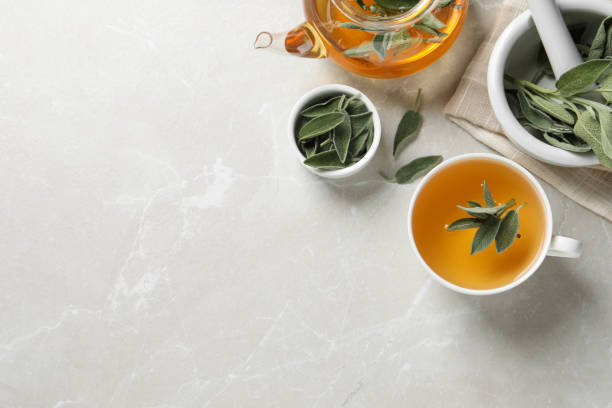istock Sage tea and green leaves on light grey marble table, flat lay. Space for text 1438637274