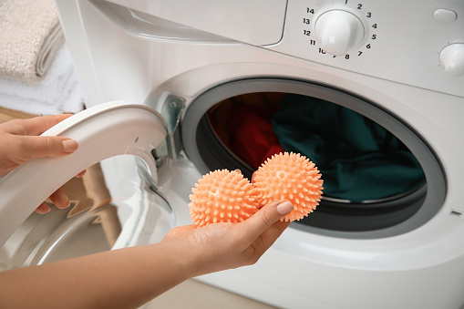 Woman putting dryer balls into washing machine, closeup