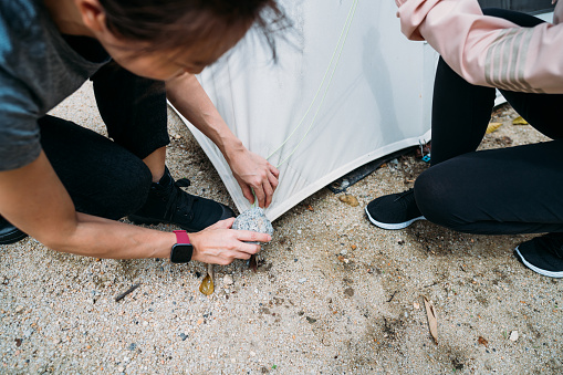 Close up of two Asian Chinese women assembling tent in the mountains, holiday outdoors camp campsite. Outdoor activity, adventure travel, or holiday vacation concept.