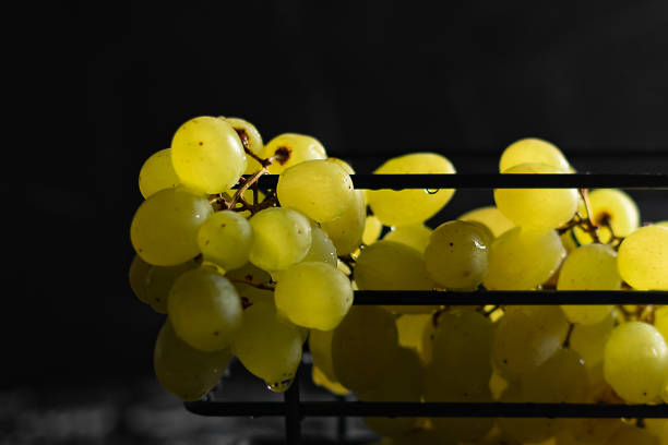 Kishmish grapes in a metal black grid stand, on a black background, in a low key, dark photo stock photo