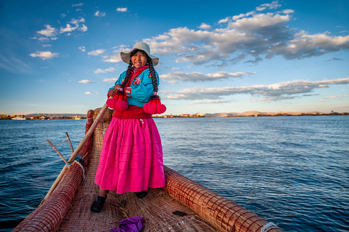 Peruvian woman sailing between Uros floating islands. Uros are a pre-Incan people that live on forty-two self-fashioned floating island in Lake Titicaca Puno, Peru and Bolivia. They form three main groups: Uru-Chipayas, Uru-Muratos  and the Uru-Iruitos. The latter are still located on the Bolivian side of Lake Titicaca and Desaguadero River. The Uros use bundles of dried totora reeds to make reed boats (balsas mats), and to make the islands themselves. The Uros islands at 3810 meters above sea level are just five kilometers west from Puno port.