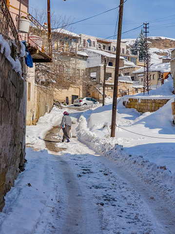 A traditional dressed female person passing a snowy winter road at the old town of Avanos (Venessa), a city close to Cappadocia (Central Anatolia, Turkey) and famous for its pottery production  industry.