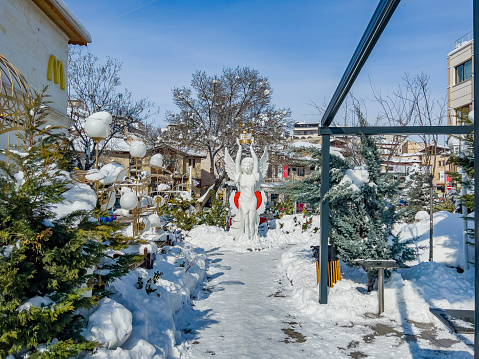 Avanos, Capadoccia Turkey - January 29th, 2022:  A white angel sculpture with wings holding a Christmas light in her hands. Outdoors of the Mc Donalds restaurant in Avanos village. Winter park scene in snow with christmas decoration.