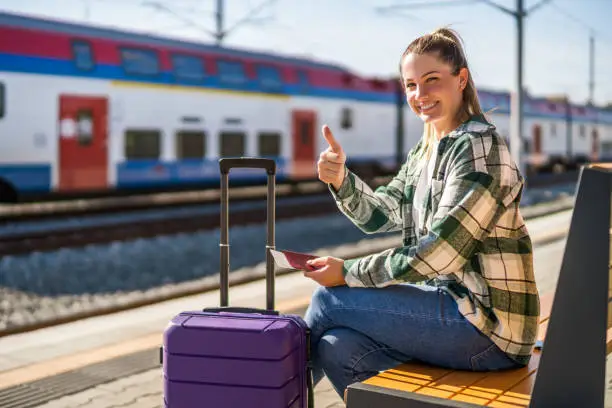 Photo of Woman showing thumb up, holding ticket and sitting on bench at the train station