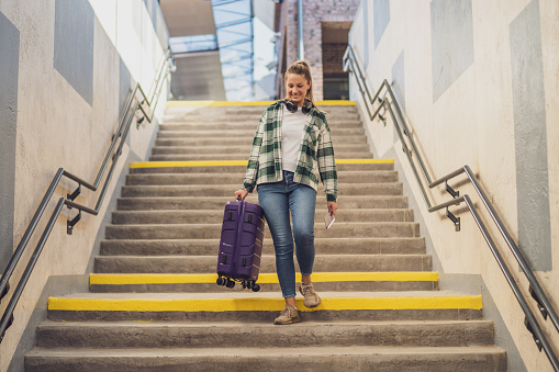 Happy woman with suitcase and ticket  walking down a stair in train station.