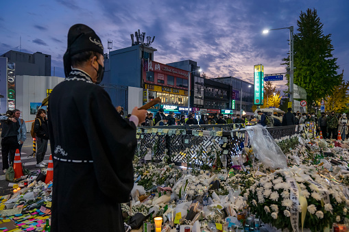 Seoul, South Korea - November 3, 2022: A priest chants at a makeshift memorial set up at an exit to Itaewon subway station, for victims of a Halloween crowd crush that occurred in an alley nearby.