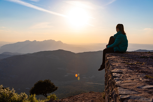 Beautiful woman sitting on an edge during sunset with mountains on the background