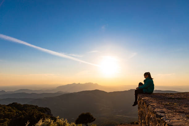 istock Beautiful woman sitting on an edge during sunset with mountains 1438665379