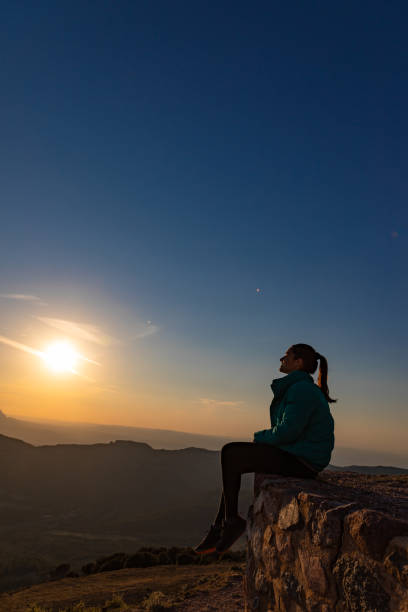 istock Beautiful woman sitting on an edge during sunset with mountains 1438665455